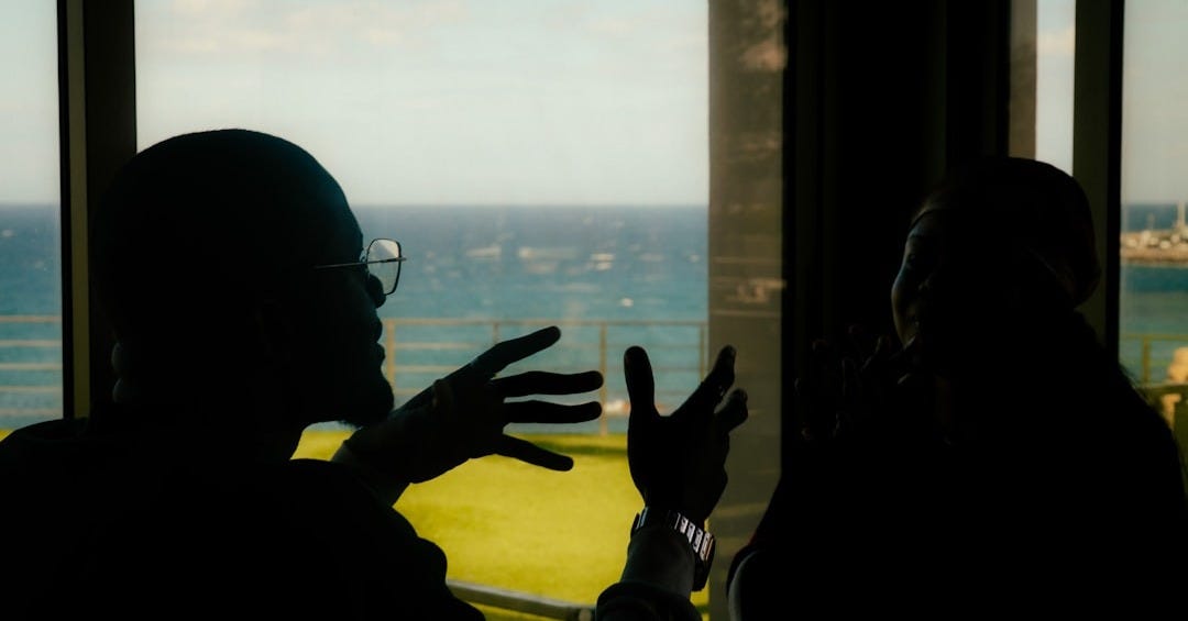 Two people silhouetted talking by a window overlooking ocean. Two people silhouetted talking by a window overlooking ocean.
