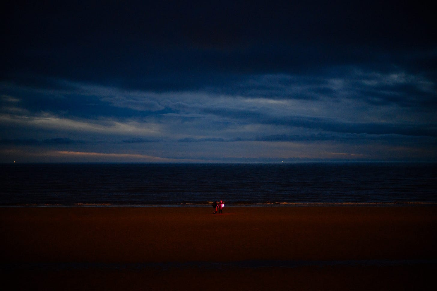 A group of people play with a purple light on the beach at dusk.