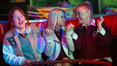 Three girls hold hands as they sit in a waltzer, laughing