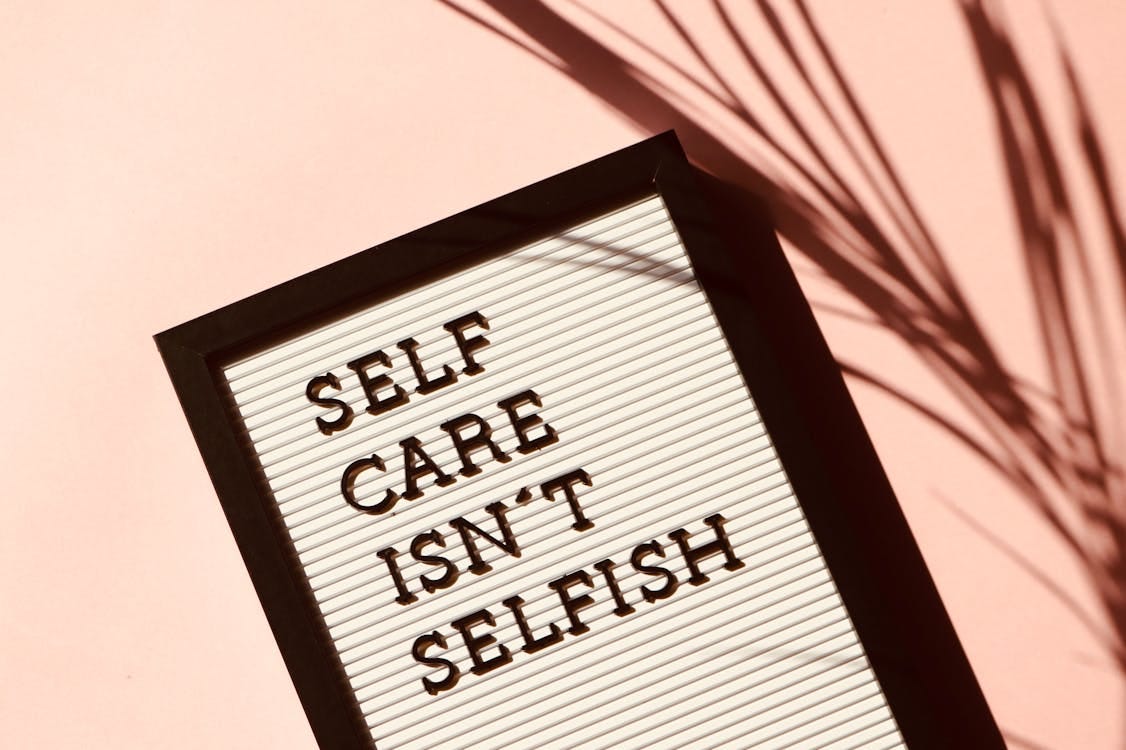 Free Letter board displaying 'Self Care Isn't Selfish' with artistic shadow on pink background. Stock Photo Free Letter board displaying 'Self Care Isn't Selfish' with artistic shadow on pink background. Stock Photo