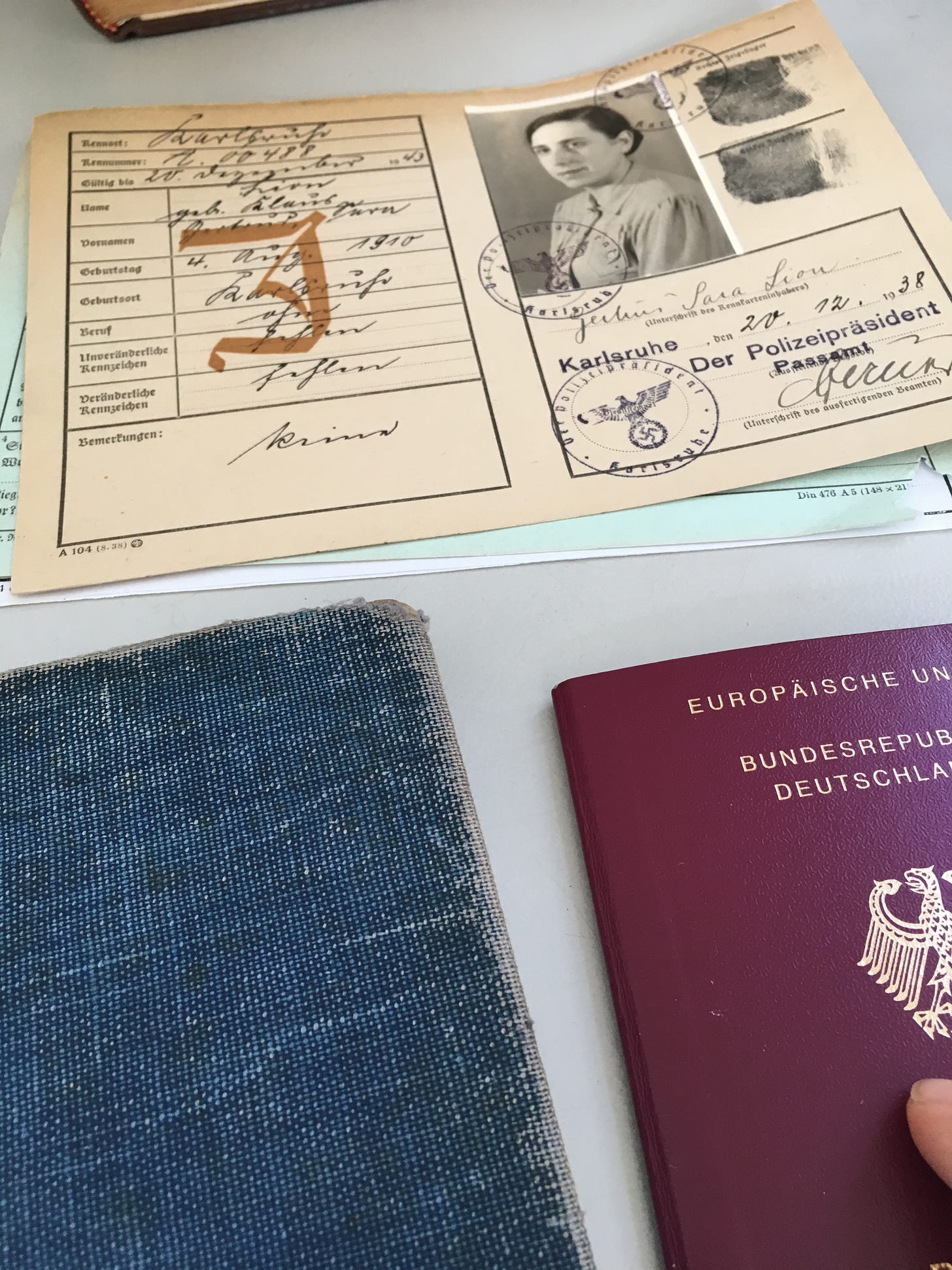 My grandmother Gertrud’s Jewish identity card in the background, foregrounded by my notebook and my closed European passport.