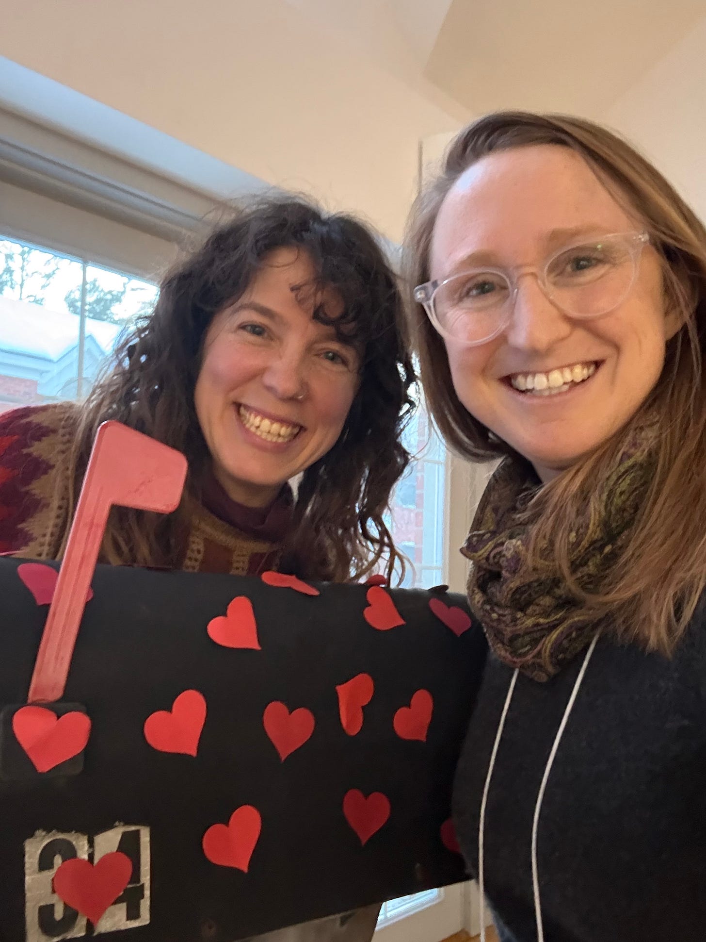 Two people smiling next to a mailbox with hearts on it.