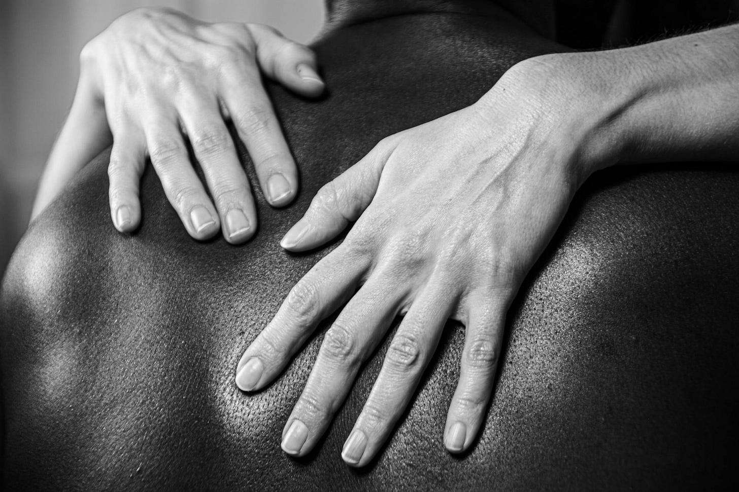 Grayscale Photo of light skinned hands embracing dark skinned back Grayscale Photo of light skinned hands embracing dark skinned back