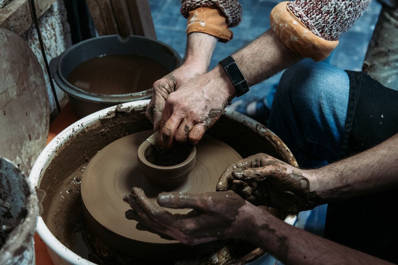 Two people shape a clay pot on a spinning pottery wheel, their hands covered in wet clay. Two people shape a clay pot on a spinning pottery wheel, their hands covered in wet clay.