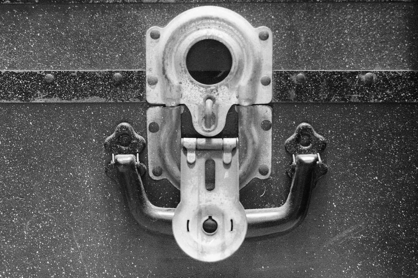 Black-and-white image of the handle and latch of a steamer trunk or footlocker. The latch is flipped open, and there's no lock in place, so the lid can be freely opened. Black-and-white image of the handle and latch of a steamer trunk or footlocker. The latch is flipped open, and there's no lock in place, so the lid can be freely opened.