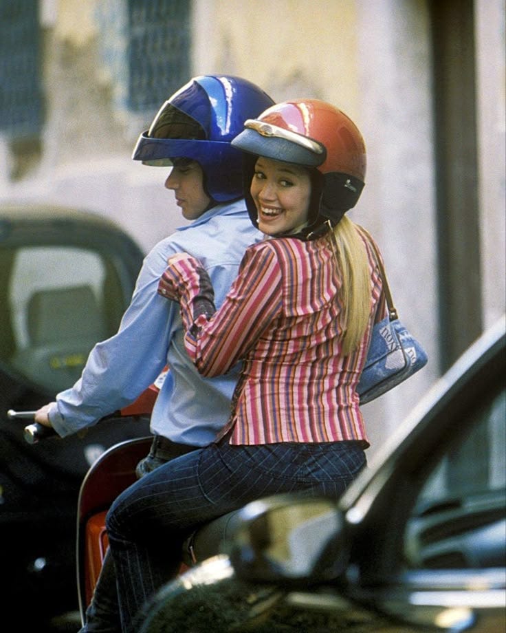 This may contain: a woman riding on the back of a motorcycle next to a man wearing a helmet