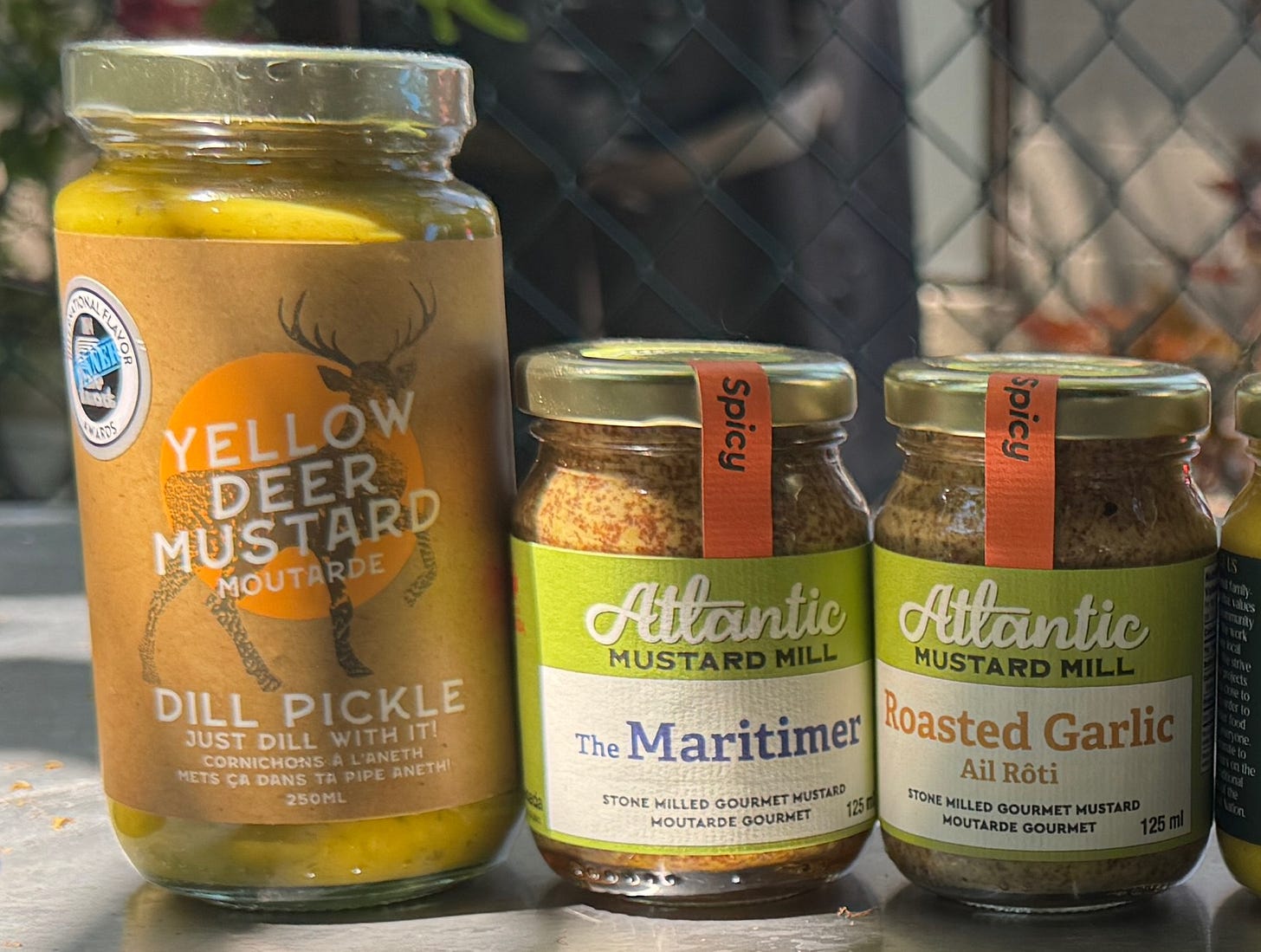 From left to right, jars and bottles as named in the caption, sitting on a metal table in a backyard. From left to right, jars and bottles as named in the caption, sitting on a metal table in a backyard.