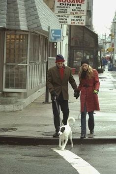This may contain: a man and woman walking their dog down the street