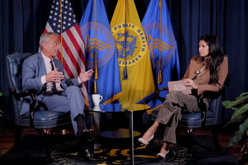 Gesundheitsminister Robert F. Kennedy Jr. sitzt in einem Sessel und spricht gestikulierend mit Podcast-Moderatorin Katie Miller. Im Hintergrund stehen die US-Flagge und Fahnen des Gesundheitsministeriums; Thema des Gesprächs sind neue US-Ernährungsrichtlinien und Kennedys Kritik an den Essgewohnheiten von Präsident Trump.