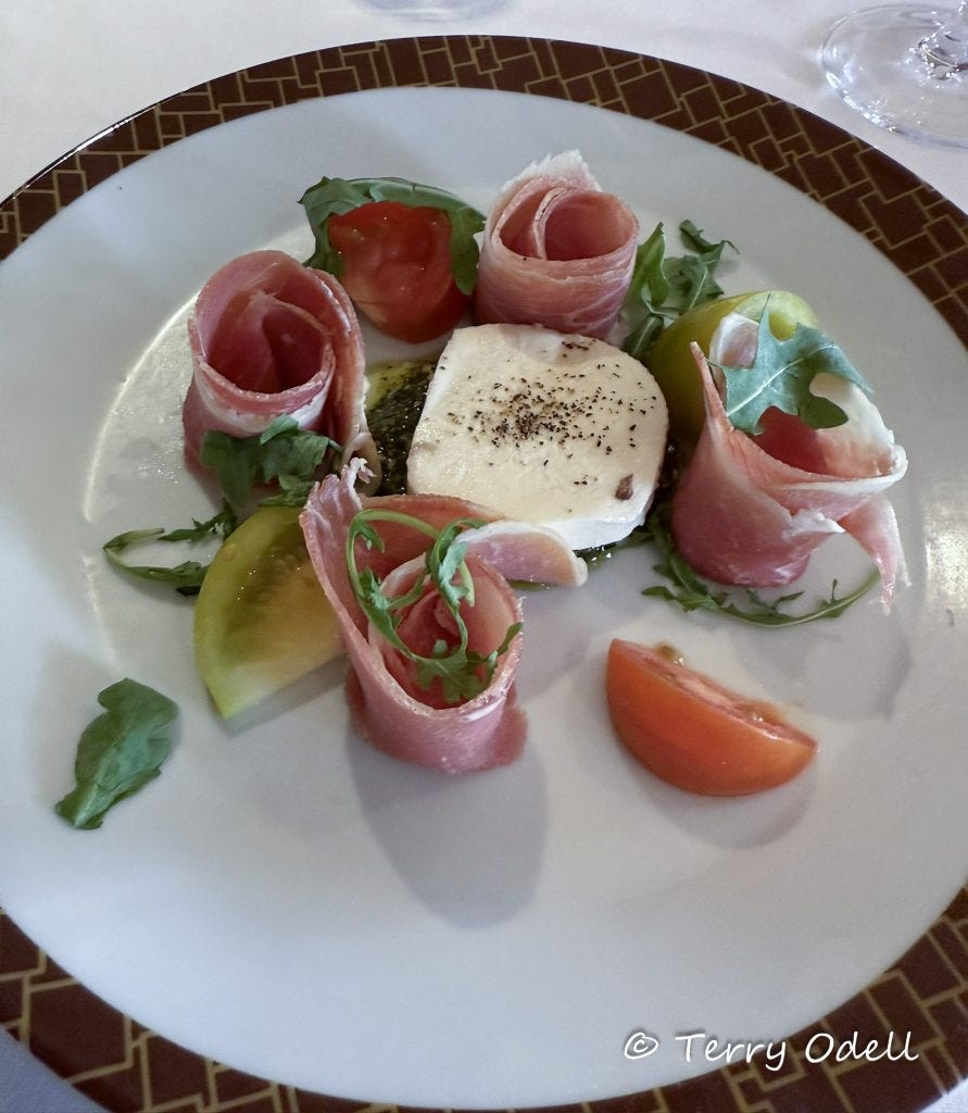 Mozzarella surrounded by curls of prosciutto with tomato slices as garnish