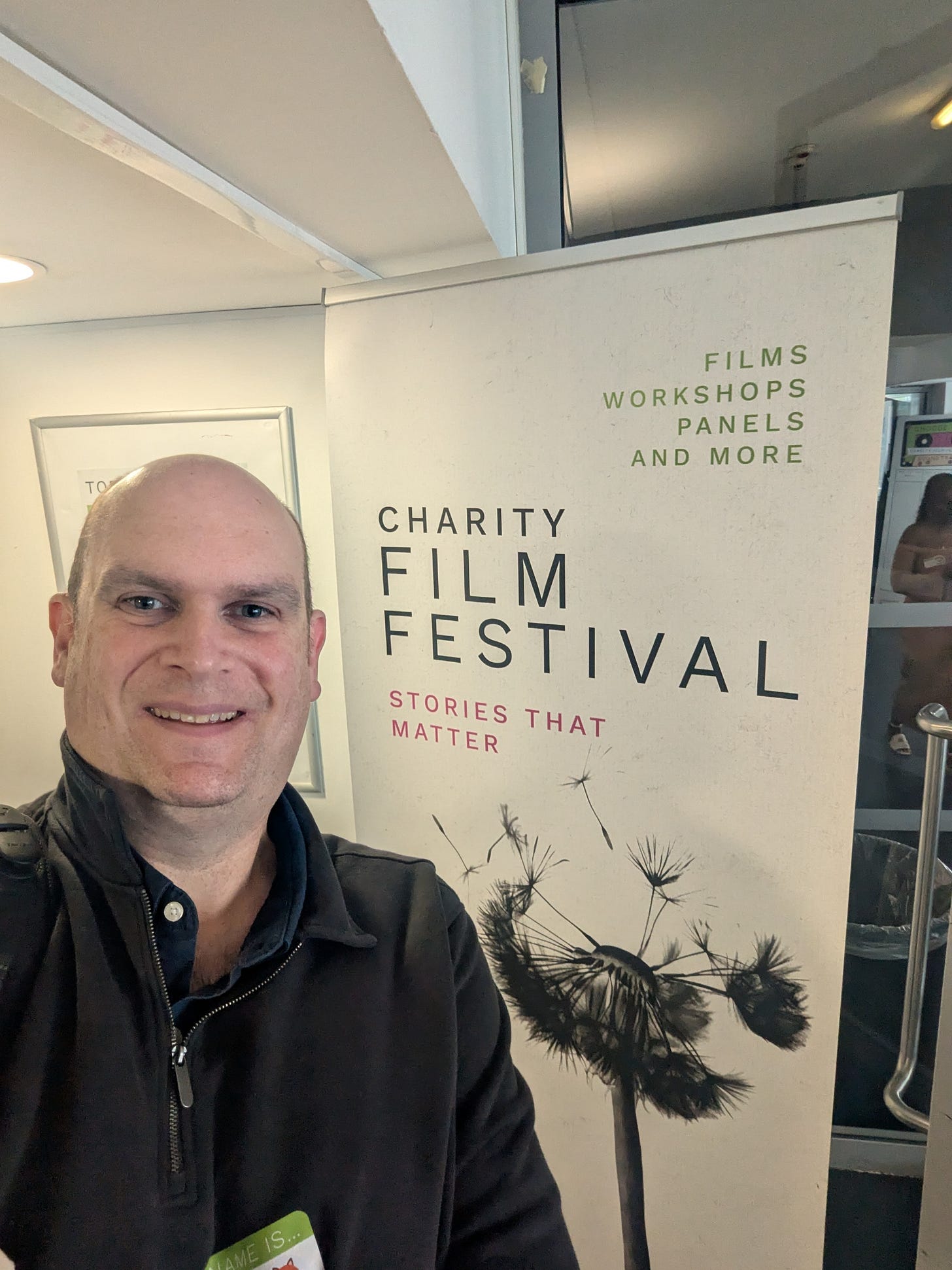 Andrew Horton (bald guy) standing next to a roll up banner saying Charity Film Festival, Stories that matter. Andrew Horton (bald guy) standing next to a roll up banner saying Charity Film Festival, Stories that matter.