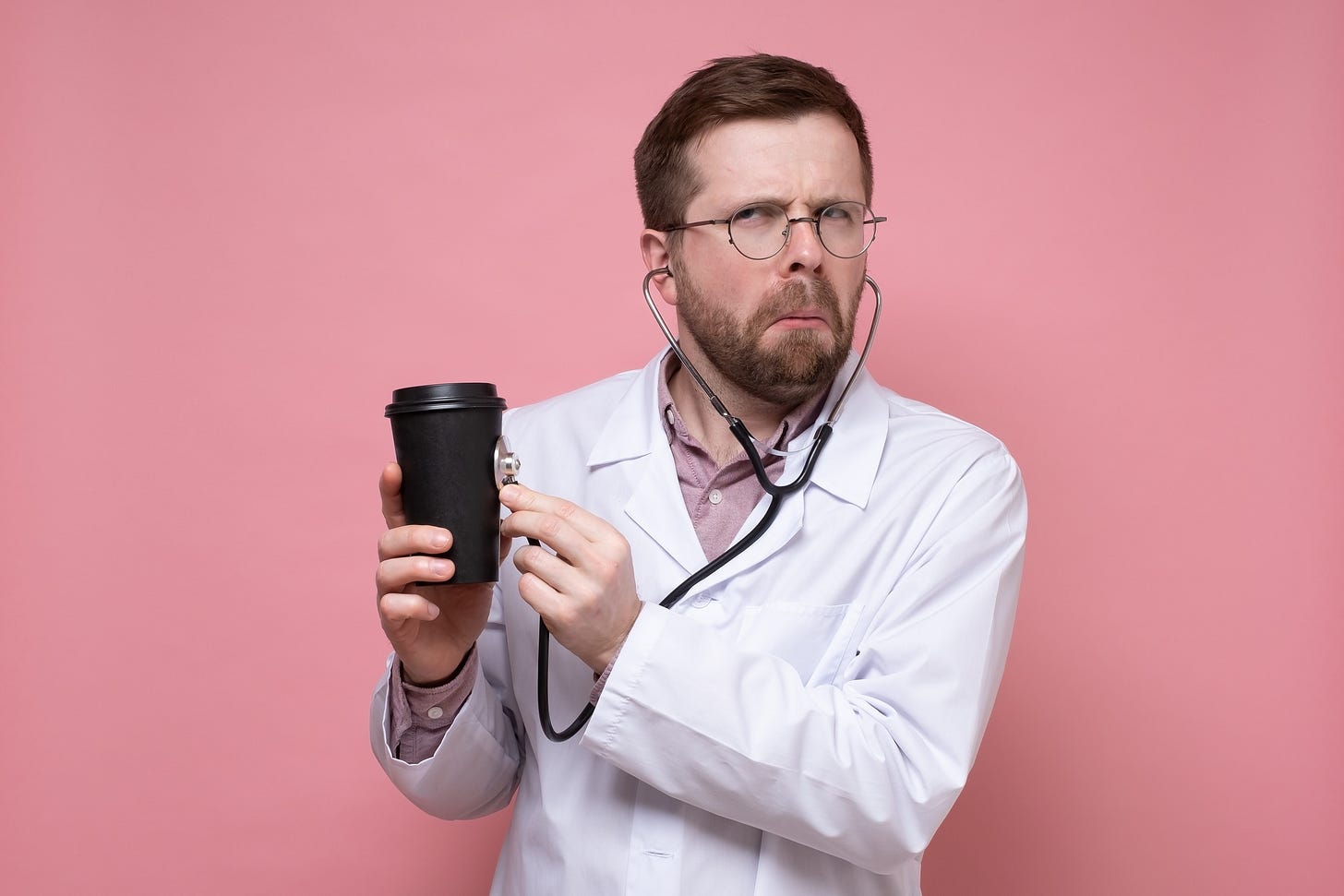 A doctor holding a stethoscope up to a coffee cup.