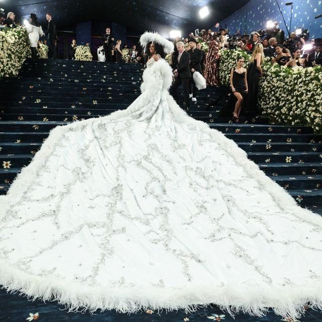 A person in a white dress with a large white feathered gown

Description automatically generated