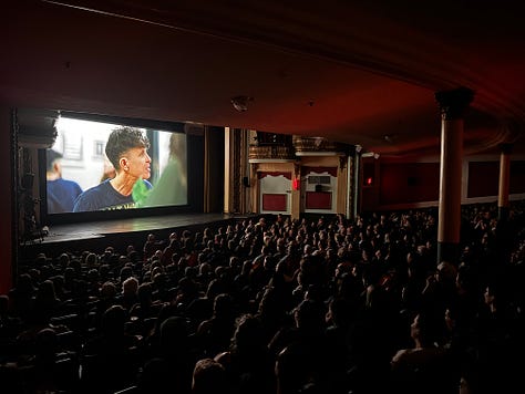 three photos of packed movie theaters screening "Come See Me in the Good Light." Giant screens with Andrea's face, or footage of Meg and Andrea hugging.