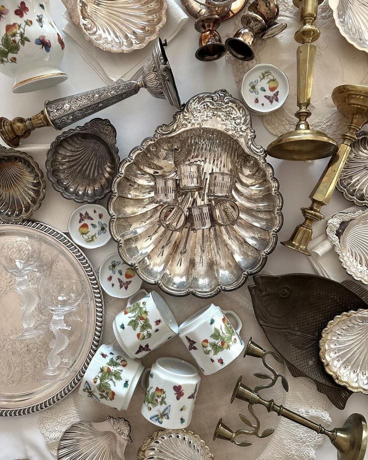 This may contain: a table topped with lots of silverware and other antique dishes on top of a white table cloth