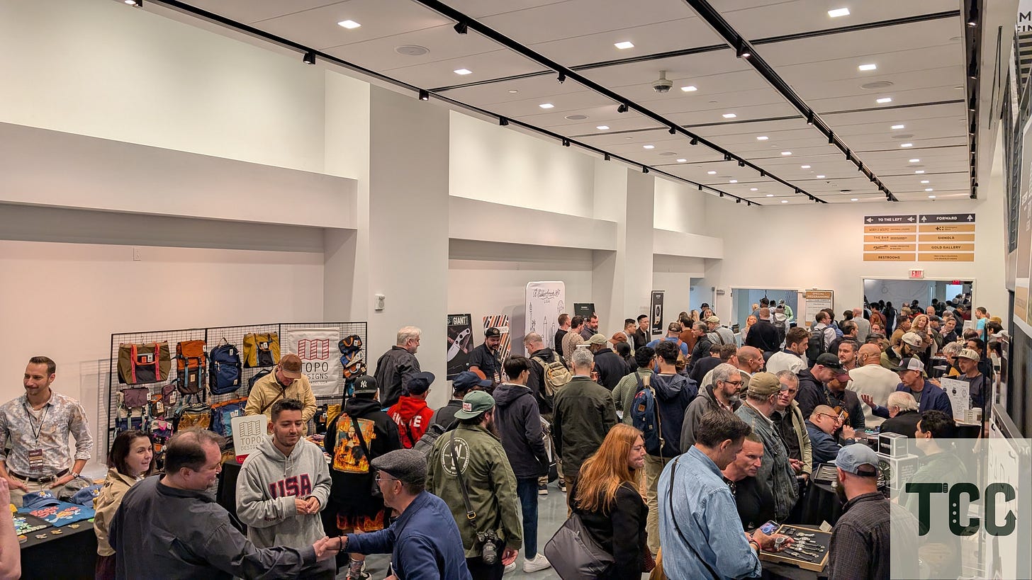 Interior shot of the first-floor vendor area at Windup Watch Fair, filled with attendees browsing booths, chatting with vendors, and inspecting products. Visible brands include Topo Designs and wristwatch strap makers.