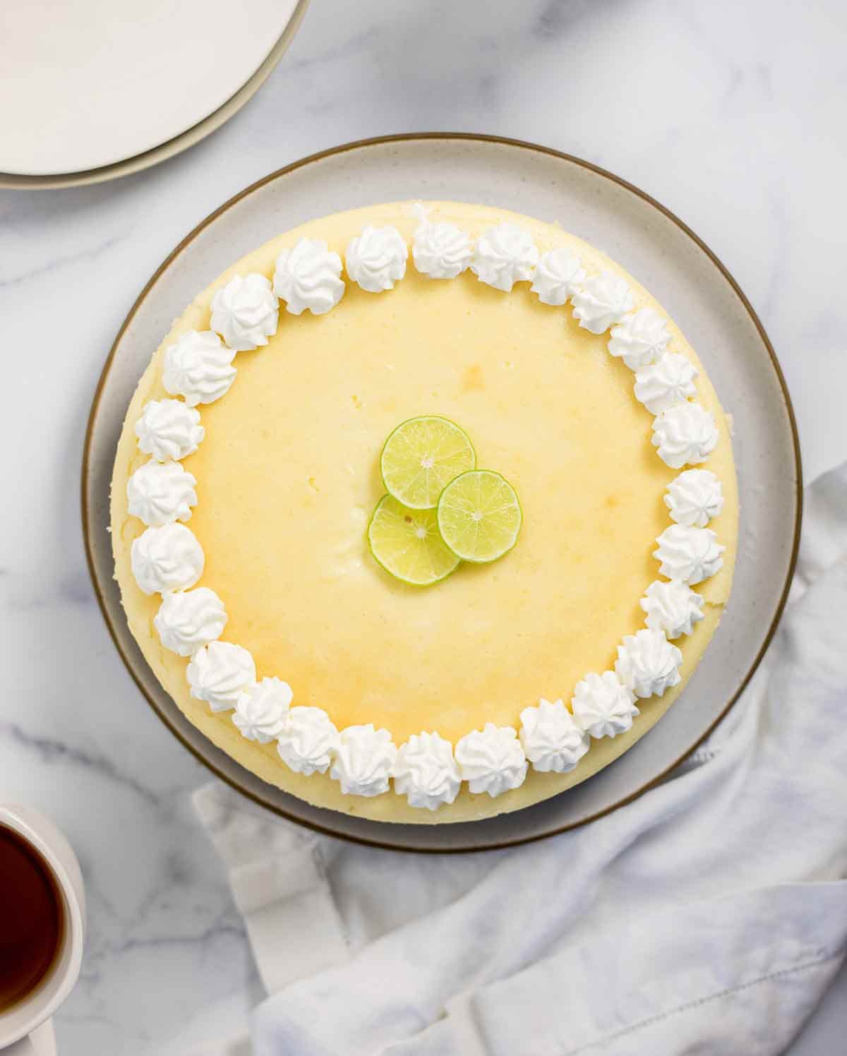 A whole key lime cheesecake garnished with whipped cream and lime zest.