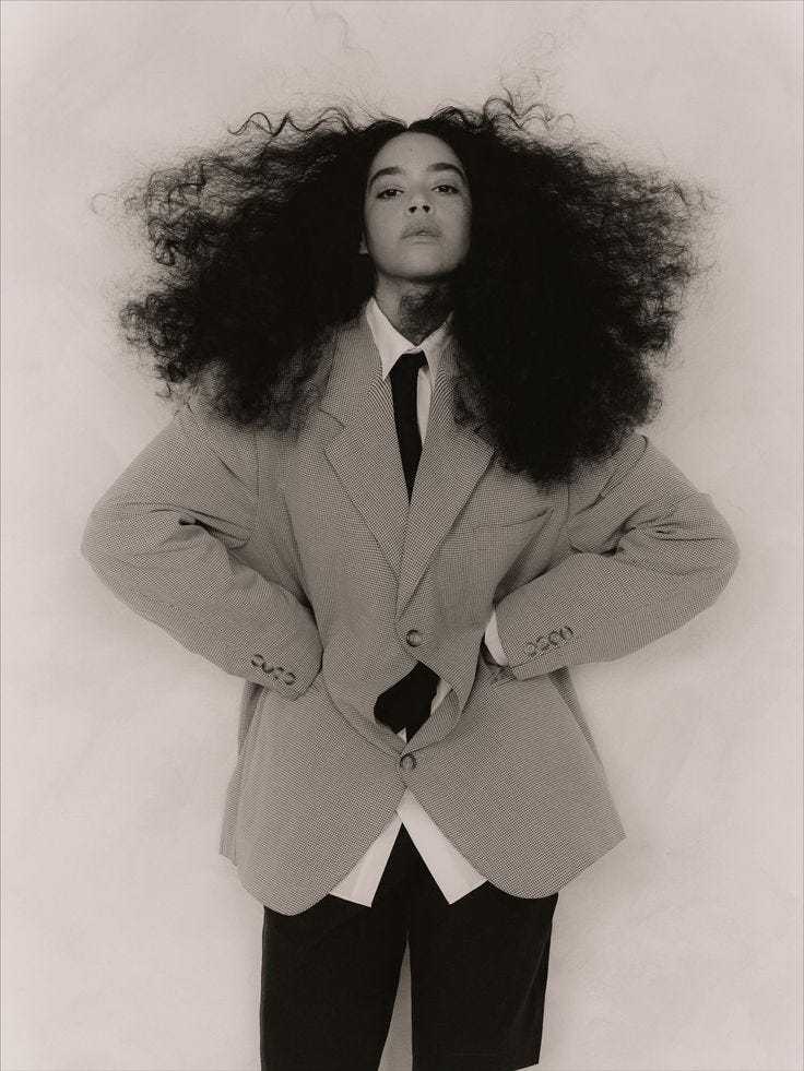 This may contain: a black and white photo of a woman wearing a suit with her hair in the air