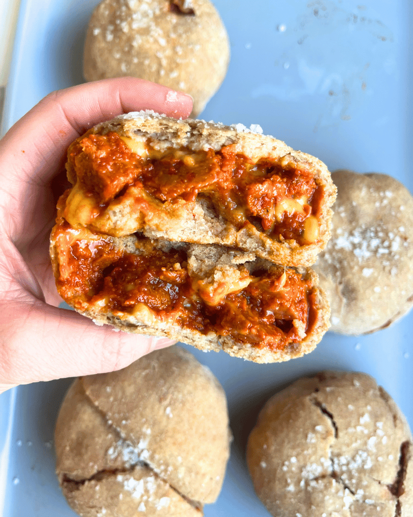 vegan pizza bun being held by a hand, open so you can see the pizza filling