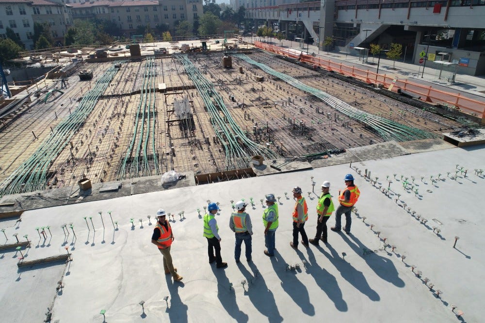 Seven contractors stand on top of a roof looking out at a commercial construction property.