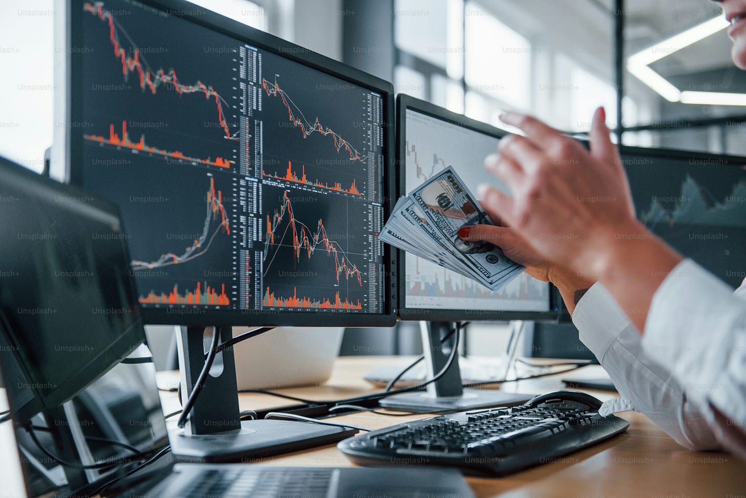 Close up view of woman's hands that holds money near the monitors with graphs.