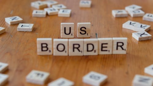 Free Scrabble tiles spelling 'US Border' on a wooden surface, symbolizing immigration themes. Stock Photo