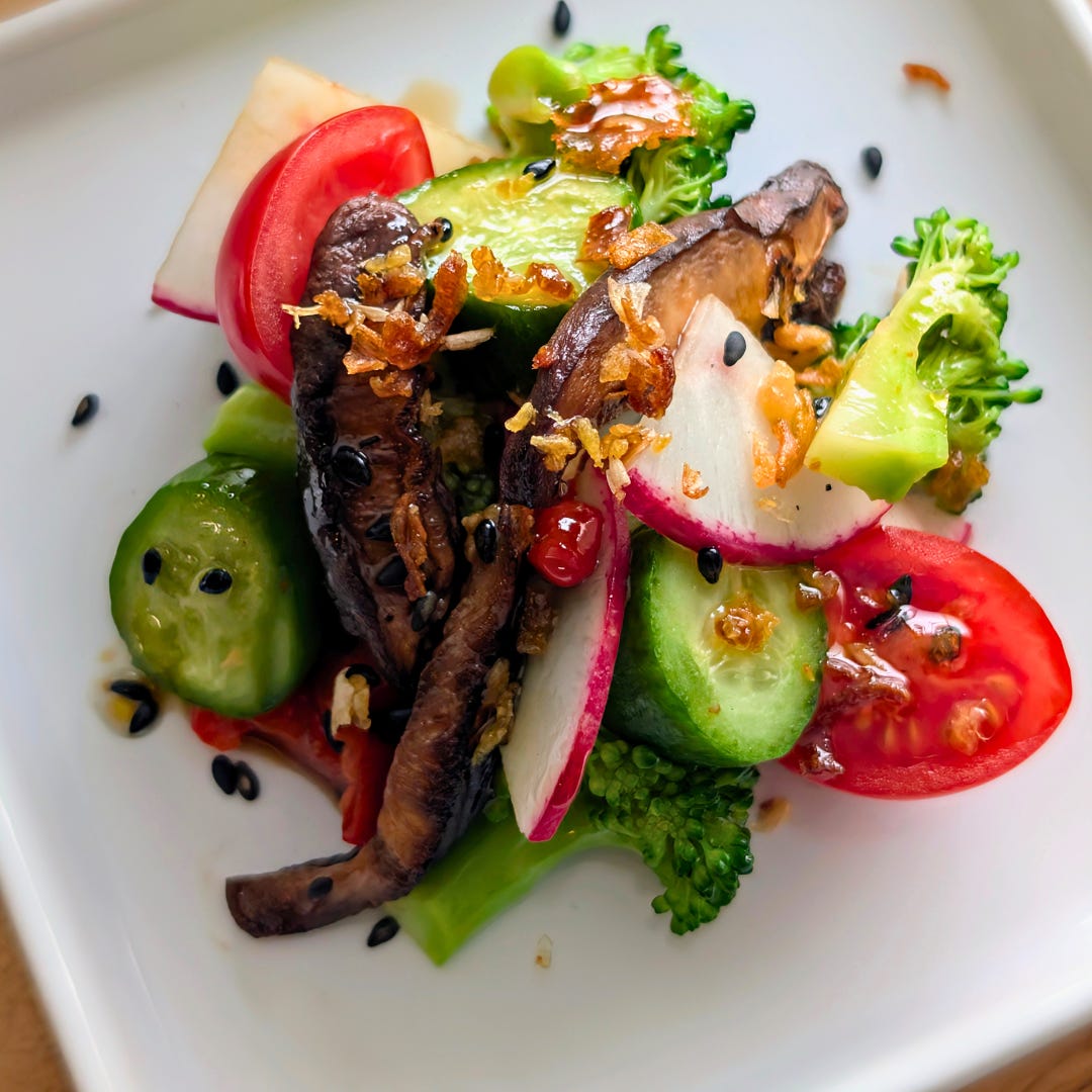 Close-up of a bite of broccoli and shiitake mushroom salad on a white plate, showing the glossy dressing and mix of textures from the roasted vegetables and crunchy toppings.
