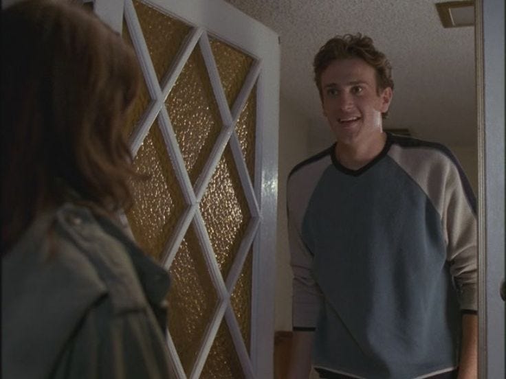 This may contain: a young man standing in front of a door talking to another person who is looking at him