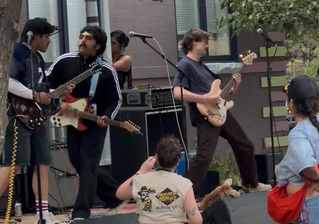 A group of musicians is performing on stage, with a guitarist, a bass player, and a drummer, while an audience watches.

AI-generated content may be incorrect.
