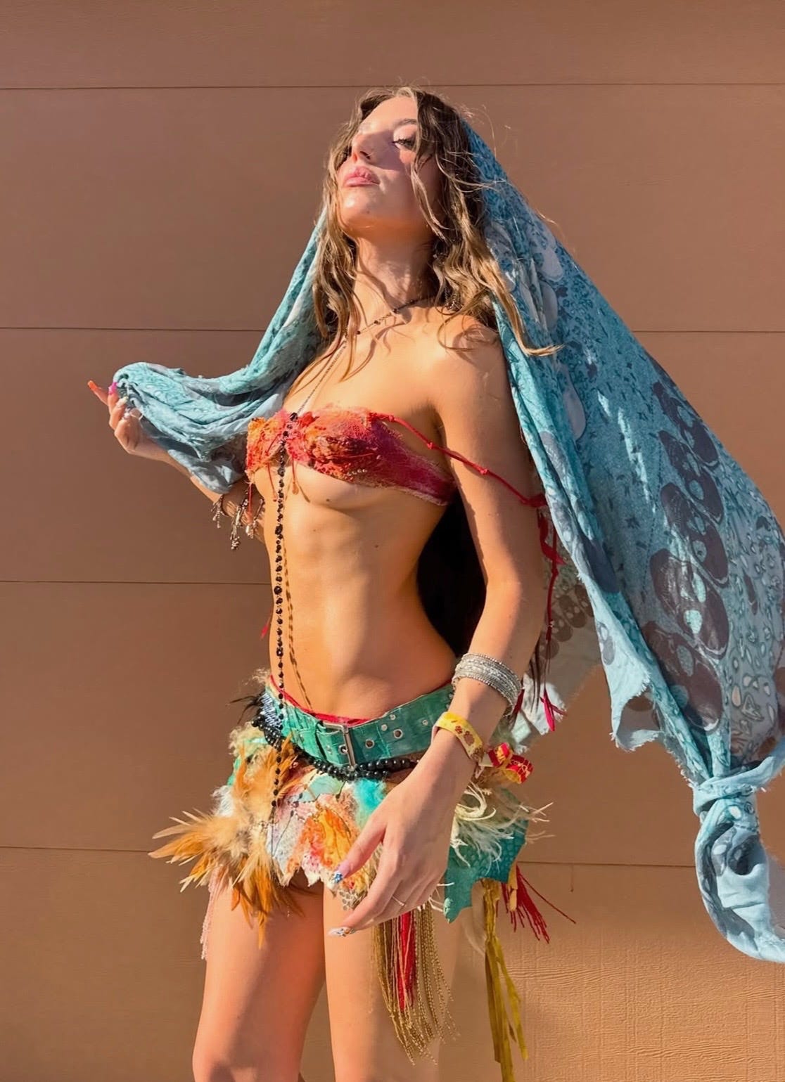 Detailed view of a custom GUVANCH festival outfit at Coachella 2026. The styling includes a textured coral bralette, a teal-studded belt, stacked silver bangles, and long layered pendant necklaces, capturing a vintage-led maximalist aesthetic.
