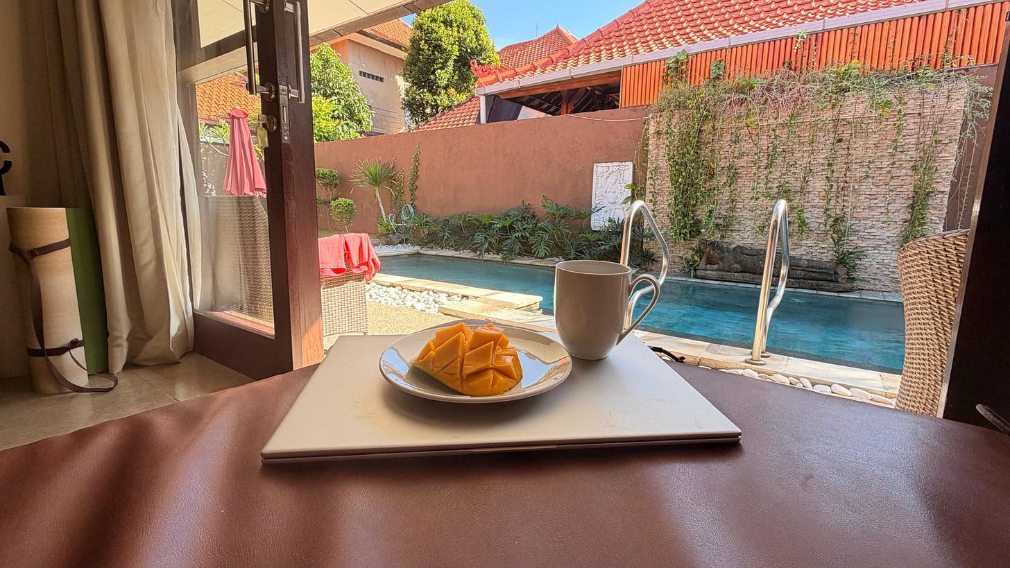 View of a pool from inside our Bali villa, with a laptop, coffee and mango.