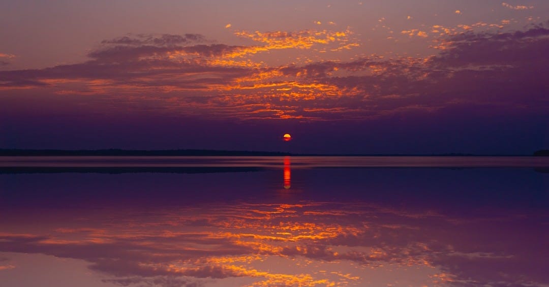 the sun is setting over the water with clouds in the sky