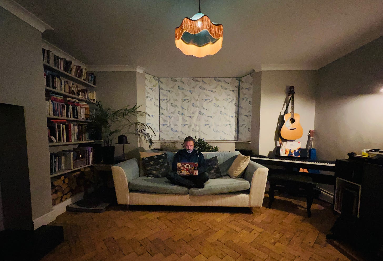A wide angle photo of a writer in his living room. sat on a sofa with a laptop. A fire crackles out of shot and a guitar hangs on the wall behind an electric piano. A wide angle photo of a writer in his living room. sat on a sofa with a laptop. A fire crackles out of shot and a guitar hangs on the wall behind an electric piano.