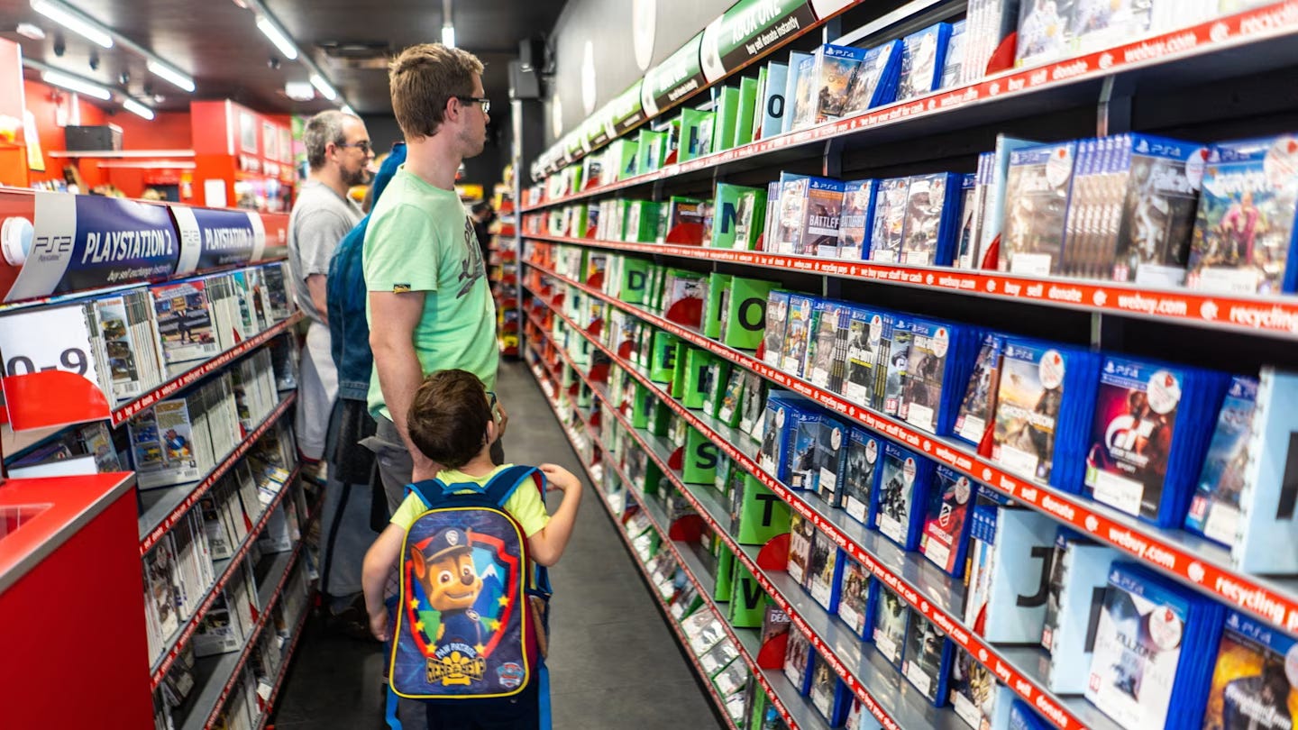 Shoppers browse shelves of video games in a brightly lit CEX store, with a child wearing a Paw Patrol backpack in the foreground. Shoppers browse shelves of video games in a brightly lit CEX store, with a child wearing a Paw Patrol backpack in the foreground.