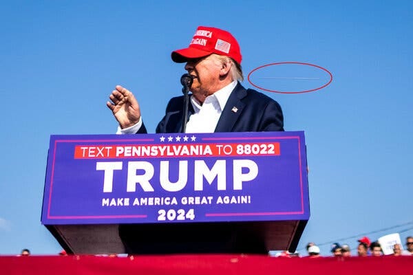 Donald Trump, in a red hat and a blue suit, speaks at a lectern. A red oval is drawn around what appears to be a bullet’s path.
