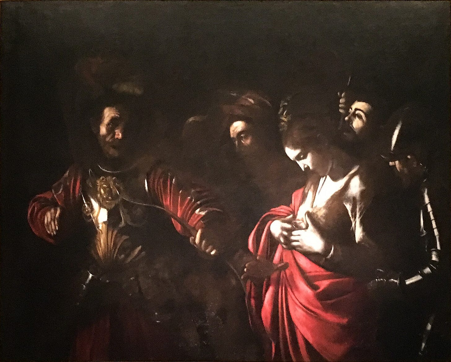 A young woman in a red robe looks down at an arrow lodged in her chest as a soldier in armor lets it fly at close range, while a pale, pained face looms behind her shoulder.