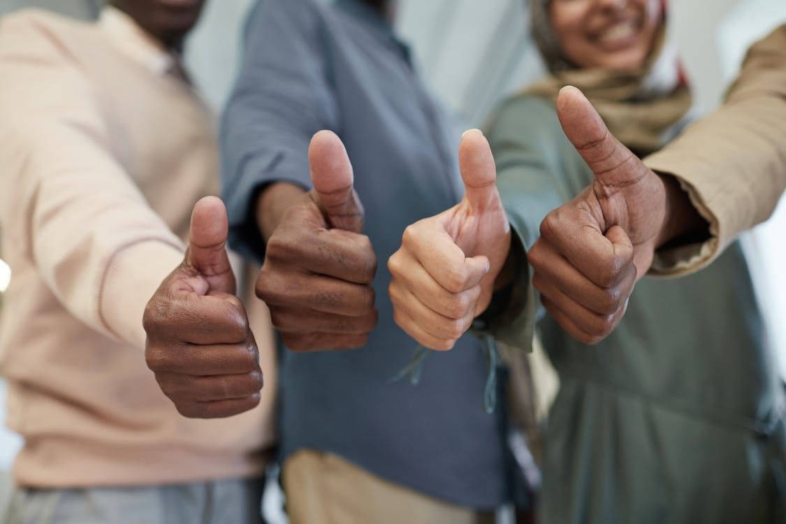 Free Close-up of a diverse team giving thumbs up indoors, symbolizing success and unity. Stock Photo