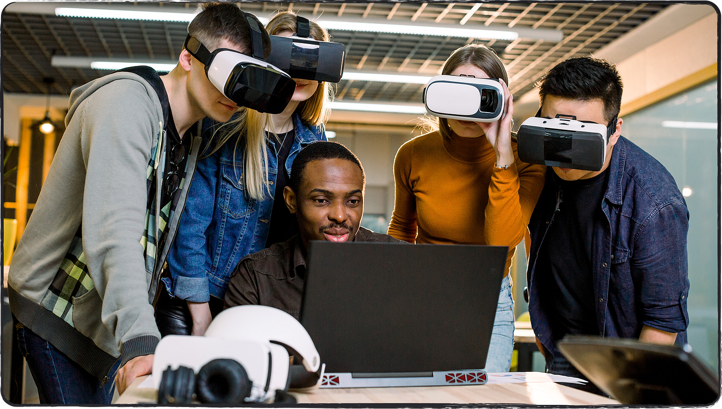 Photo showing young tech workers using VR headsets, gathered around a desk!