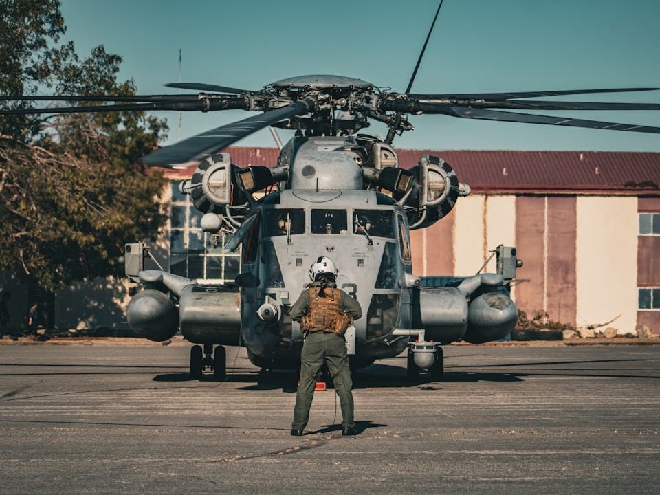 Pilot stands before a large military helicopter on tarmac