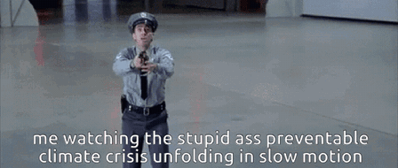GIF of a uniformed police officer aiming a pistol straight ahead in a large empty hall. Text: "me watching the stupid ass preventable climate crisis unfolding in slow motion"