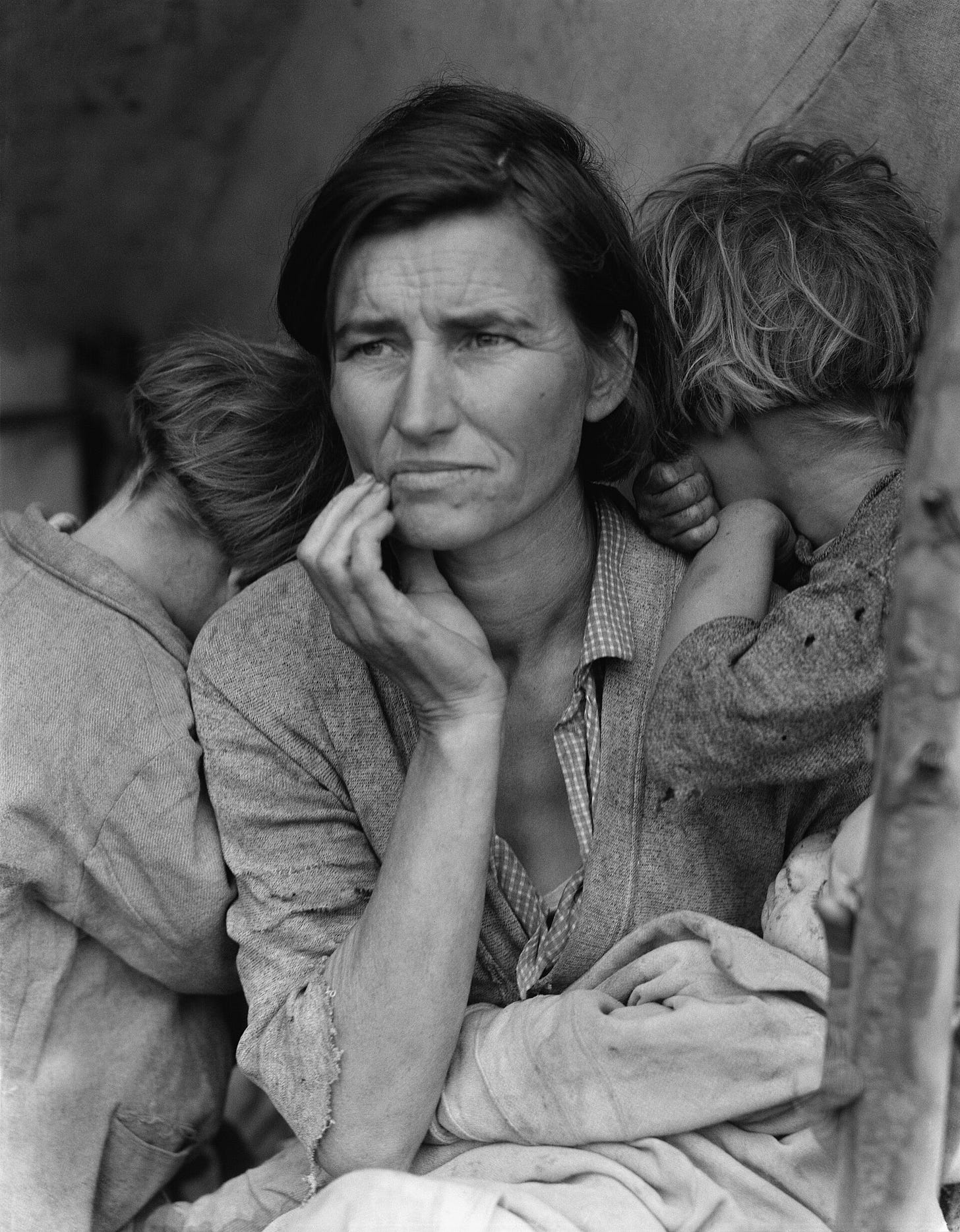 Black-and-white photograph of a worried woman with her hand at her chin, two children hiding their faces against her shoulders and a baby in her lap. Black-and-white photograph of a worried woman with her hand at her chin, two children hiding their faces against her shoulders and a baby in her lap.