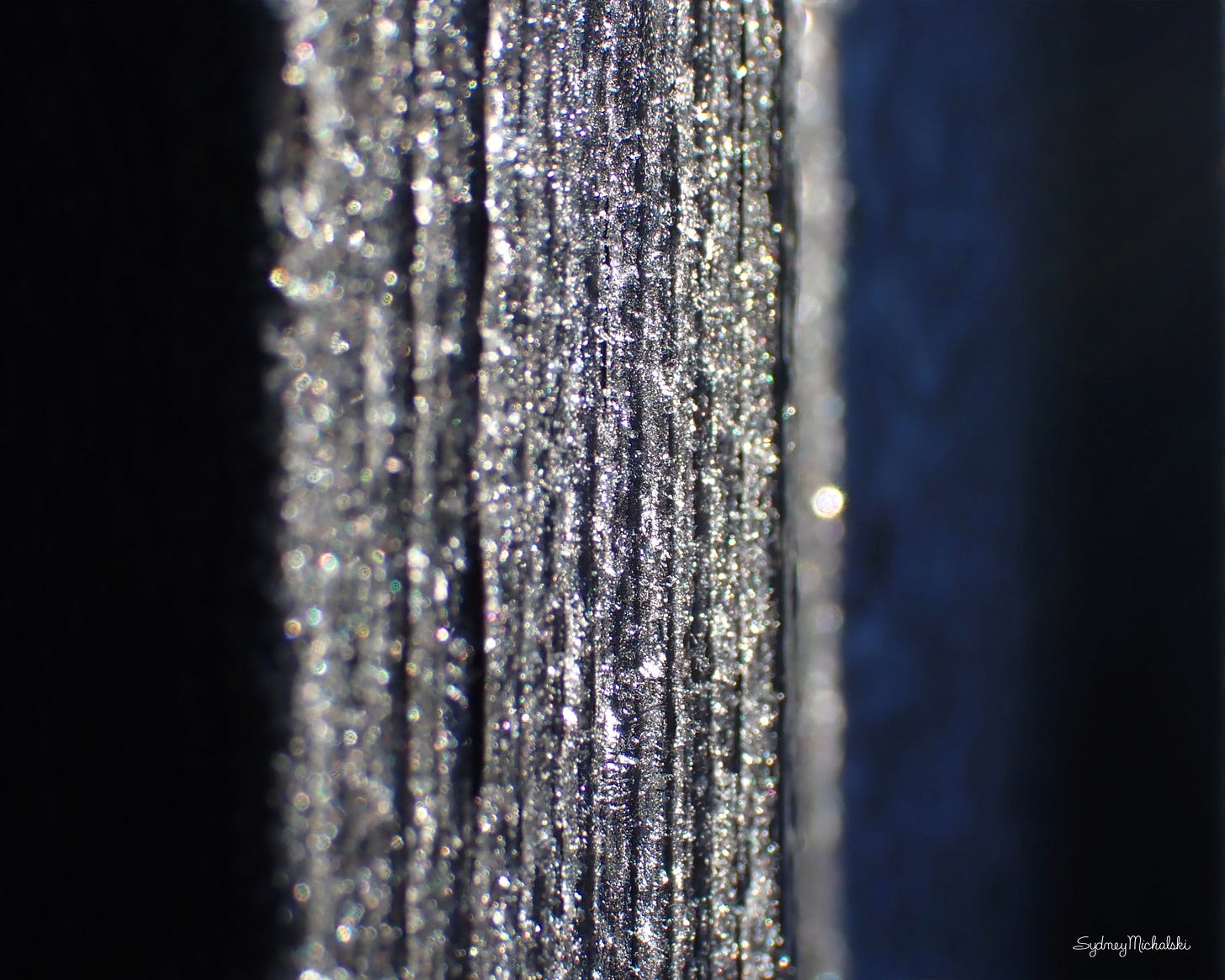 A naturally abstract photograph features centered vertical stripes of glittering white fading into a black background on each side.