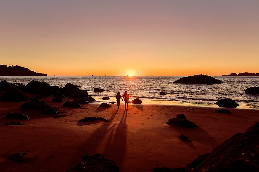 a couple walking on the beach during sunset.