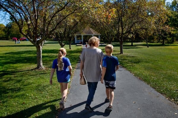 MaryBeth walking on a path through a park with a child on each side of her.