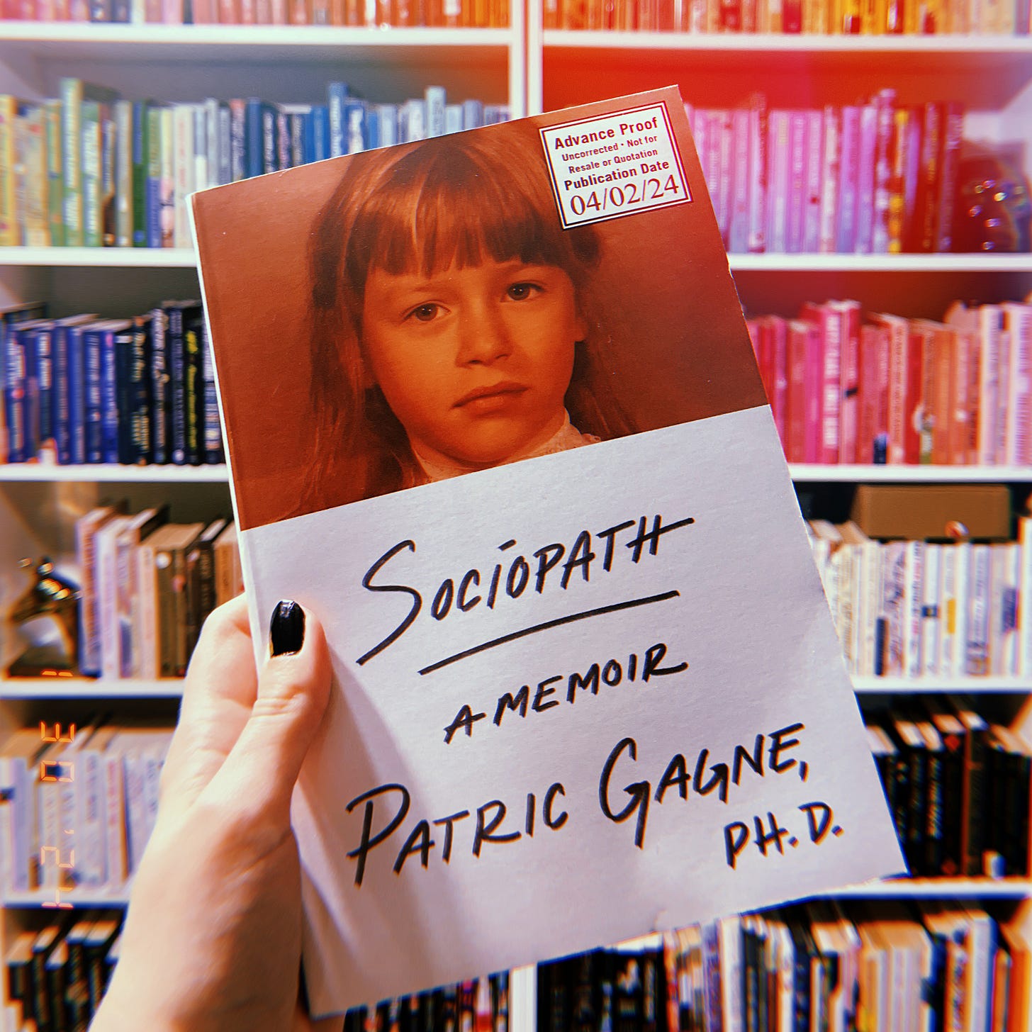 A hand holding up an advanced reader copy of Sociopath: A Memoir by Patric Gagne. Behind is a colorful bookshelf. A hand holding up an advanced reader copy of Sociopath: A Memoir by Patric Gagne. Behind is a colorful bookshelf.