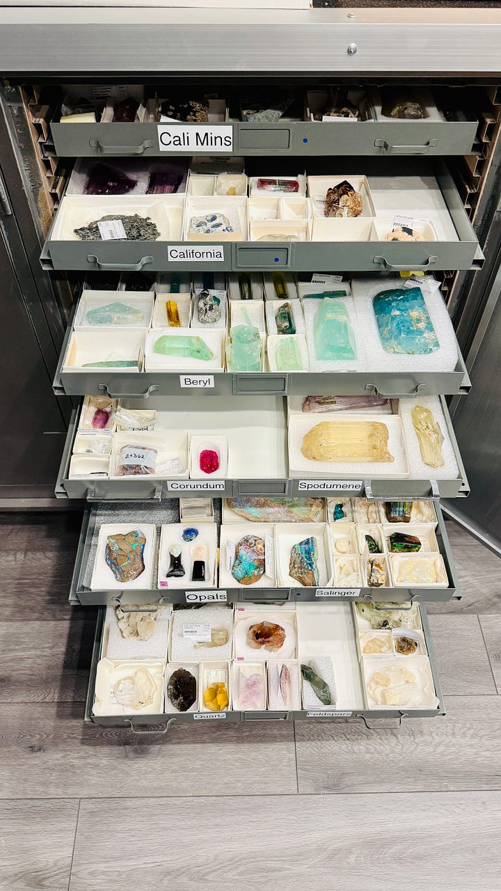 Open specimen drawers in the mineral research collection at the Natural History Museum of Los Angeles County, showing rows of labeled minerals including beryl, corundum, spodumene, opals, quartz, and feldspar, each specimen boxed and catalogued.
