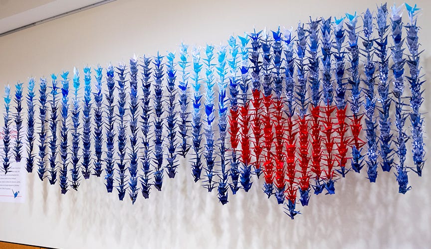 Origami cranes in different color shades hanging in rows across a hospital corridor.