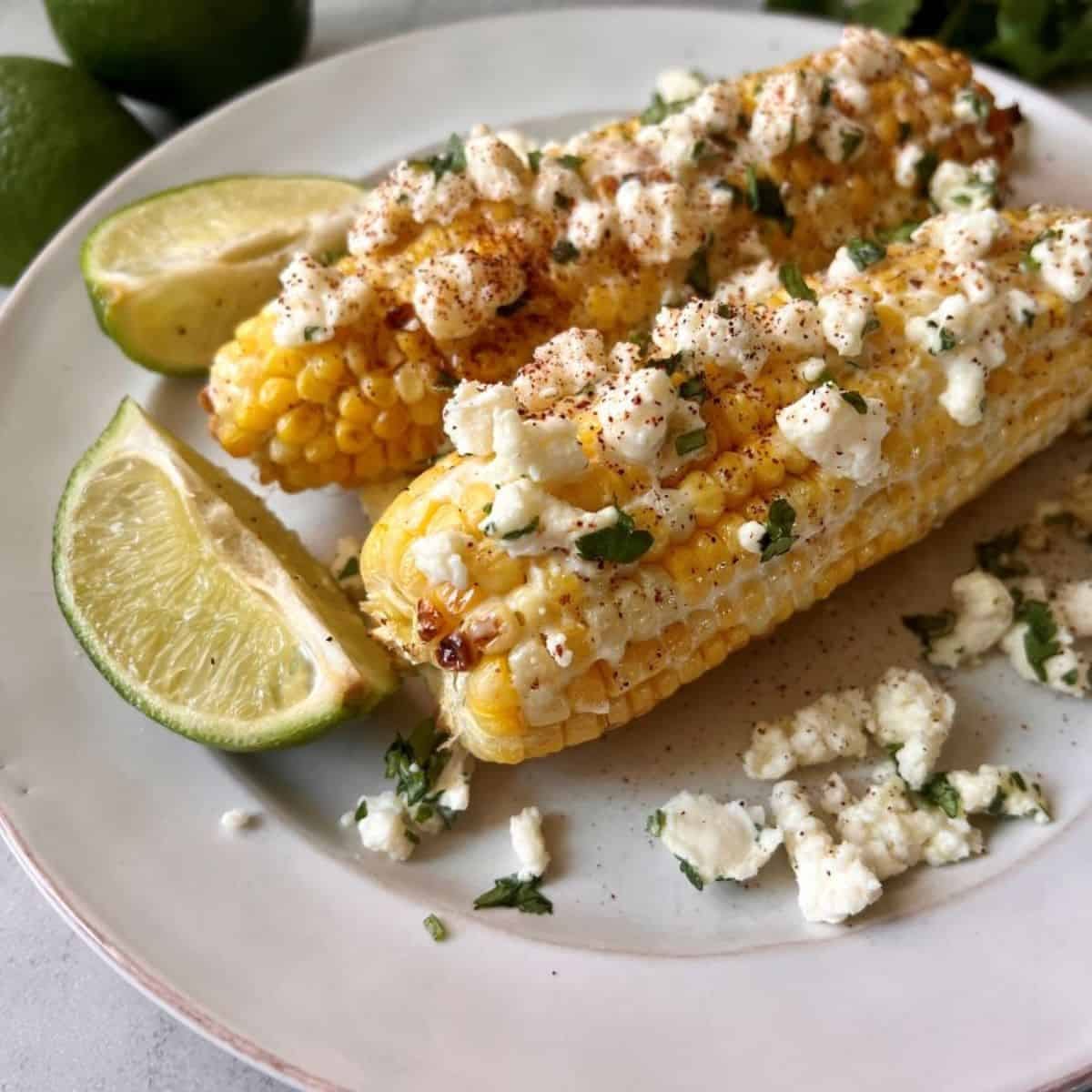 Elote on a white plate with lime wedges