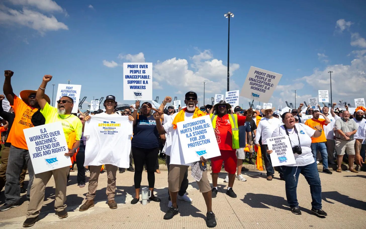 A multiracial group of dockworkers on strike with signs and t-shirts sporting pro-union slogans.