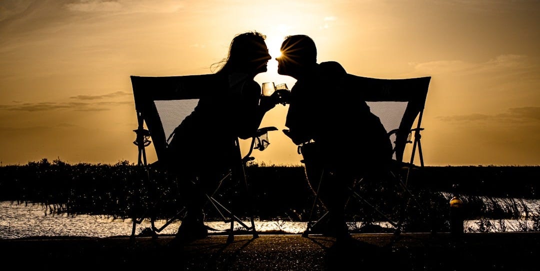 a couple of people sitting on a bench with a sunset in the background a couple of people sitting on a bench with a sunset in the background